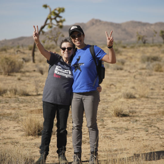 Two small humans giving the peace sign while wearing Hamilton the musical shirts, in the Joshua Tree desert